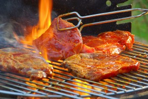 Fleisch auf dem Grill wird mit einer Grillzange gewendet