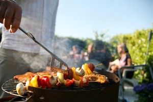 Ein Schaschlikspieß wird mithilfe einer Grillzange gewendet